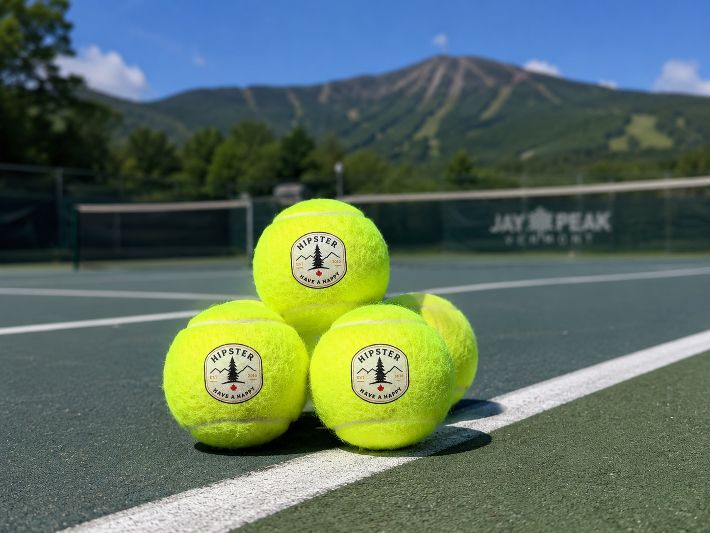 Hipster Vermont branded tennis balls stacked on the Jay Peak tennis court with the mountain in the background